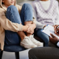 Close up of African-American psychologist taking notes on clipboard in therapy session for children